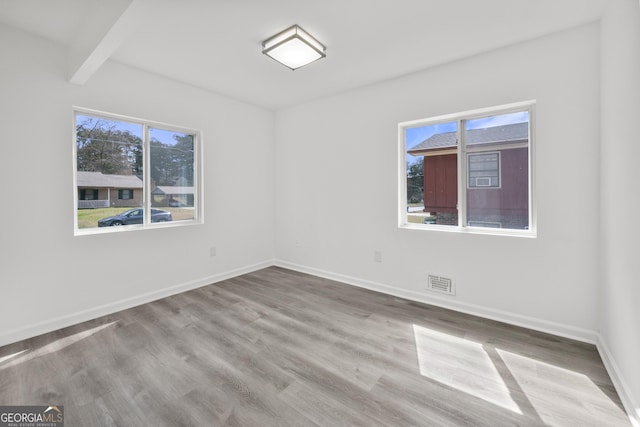 spare room featuring wood finished floors, baseboards, a healthy amount of sunlight, and visible vents