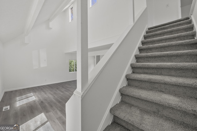 staircase featuring visible vents, baseboards, a towering ceiling, and wood finished floors