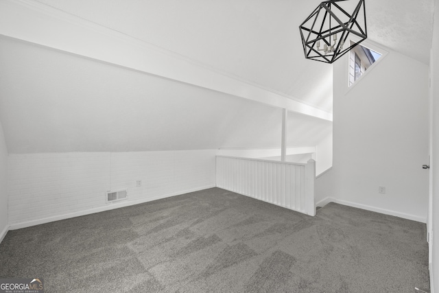 additional living space featuring lofted ceiling, dark colored carpet, brick wall, baseboards, and visible vents