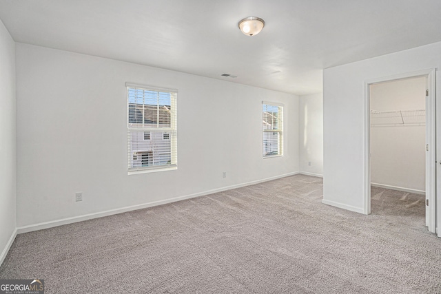 unfurnished bedroom featuring light carpet, multiple windows, a spacious closet, and baseboards