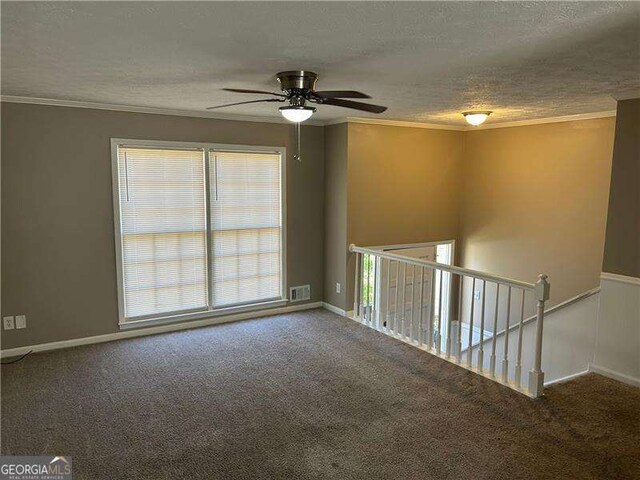 empty room featuring visible vents, ornamental molding, a textured ceiling, carpet flooring, and ceiling fan