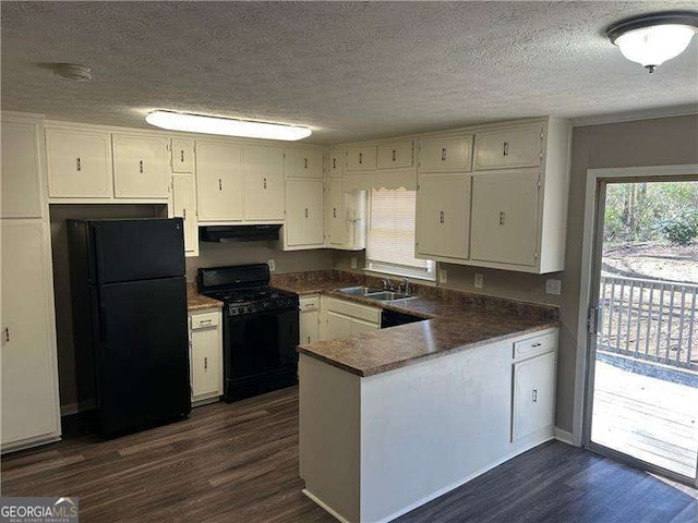 kitchen featuring dark countertops, under cabinet range hood, a peninsula, black appliances, and a sink