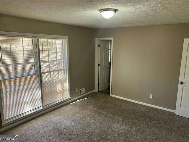 spare room with visible vents, a textured ceiling, baseboards, and dark colored carpet