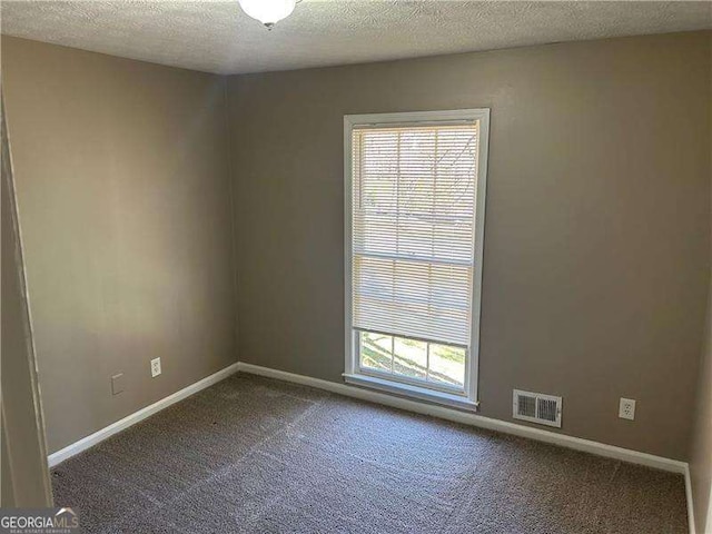 empty room with visible vents, carpet flooring, a textured ceiling, and baseboards