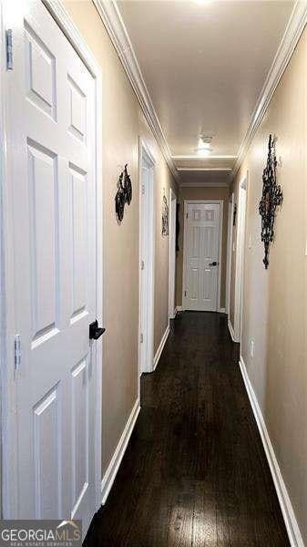 corridor featuring crown molding, dark wood-style floors, and baseboards