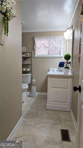 bathroom with visible vents, baseboards, toilet, ornamental molding, and vanity
