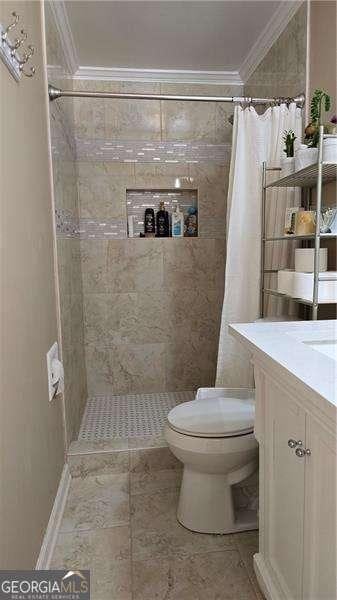 bathroom with tiled shower, toilet, ornamental molding, and vanity