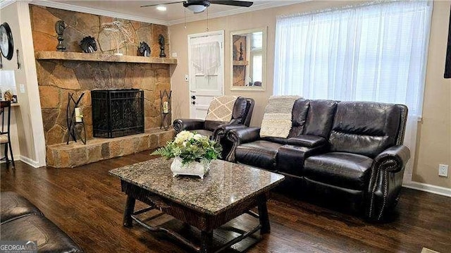 living area featuring baseboards, ornamental molding, a stone fireplace, wood finished floors, and a ceiling fan