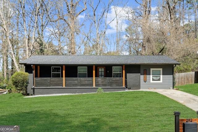 view of front facade with a porch, a front yard, brick siding, roof with shingles, and fence