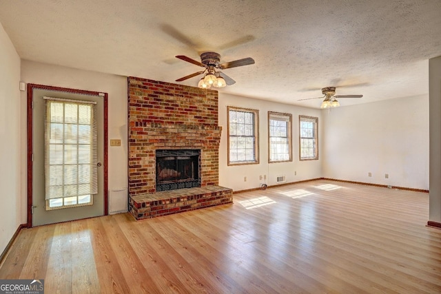 unfurnished living room with wood finished floors, a ceiling fan, baseboards, a textured ceiling, and a brick fireplace