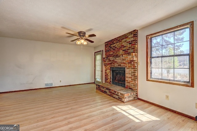 unfurnished living room featuring wood finished floors, visible vents, ceiling fan, a textured ceiling, and a brick fireplace