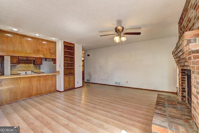 unfurnished living room featuring visible vents, a brick fireplace, ceiling fan, and light wood finished floors