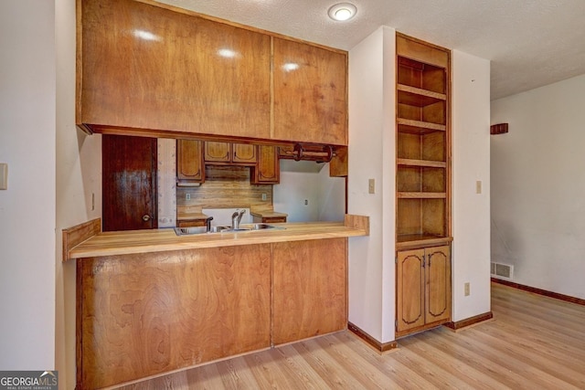 kitchen with baseboards, visible vents, light wood finished floors, a sink, and brown cabinets