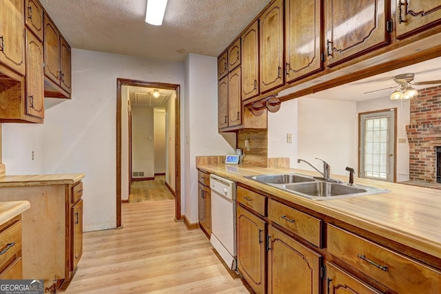 kitchen featuring brown cabinetry, a sink, light wood-style floors, a textured ceiling, and dishwasher