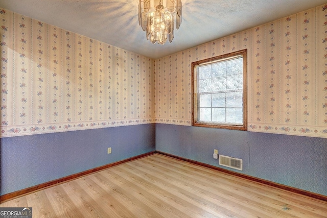 spare room featuring a chandelier, visible vents, wallpapered walls, and wood finished floors