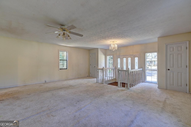 carpeted spare room featuring ceiling fan with notable chandelier and a textured ceiling