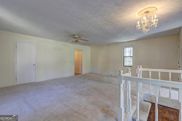 carpeted empty room featuring a textured ceiling and ceiling fan with notable chandelier