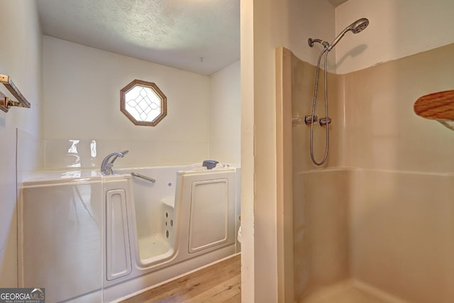 bathroom with wood finished floors, a textured ceiling, walk in shower, and a bath