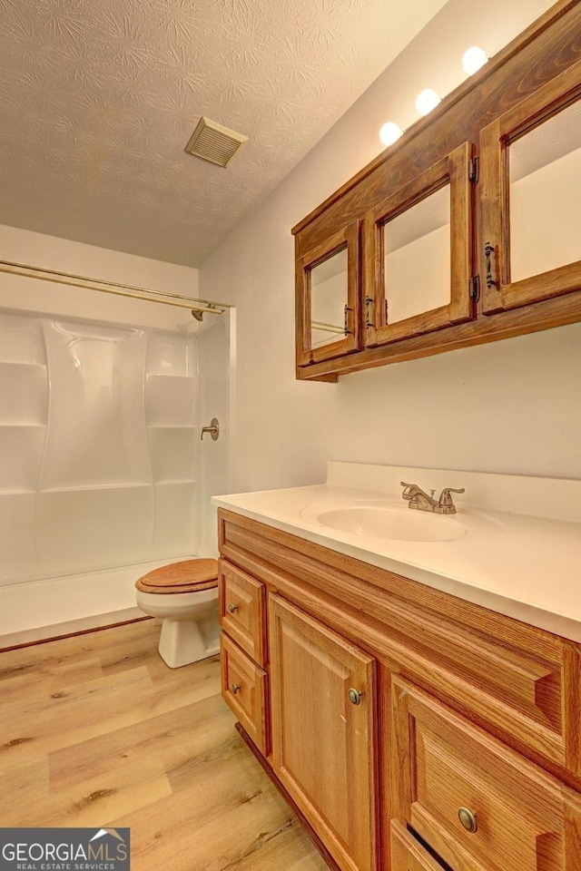 bathroom featuring vanity, wood finished floors, walk in shower, a textured ceiling, and toilet