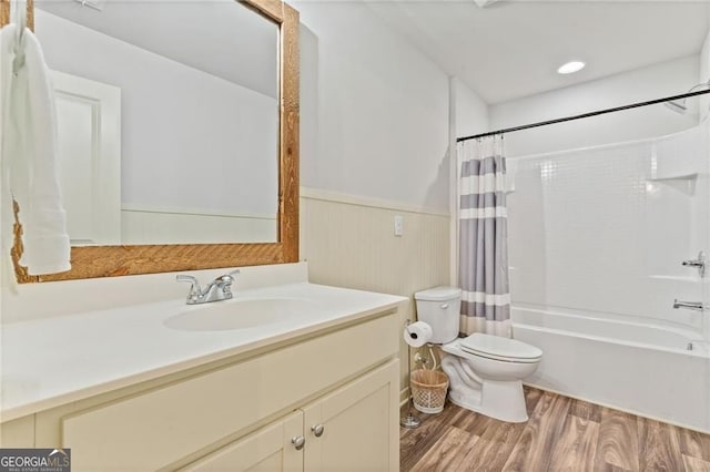 bathroom featuring a wainscoted wall, toilet, wood finished floors, shower / bathtub combination with curtain, and vanity