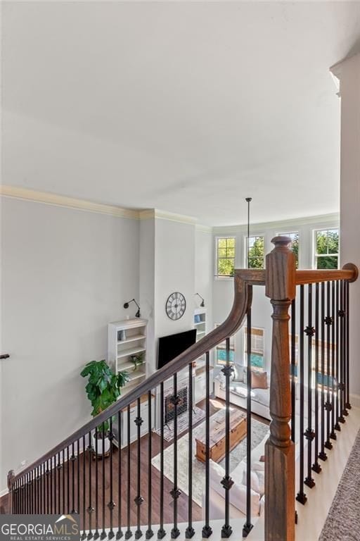 hall featuring an upstairs landing, baseboards, crown molding, and wood finished floors