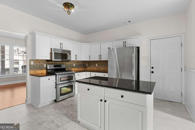 675 Timber Ives Dr, Dacula, GA 30019 - kitchen featuring appliances with stainless steel finishes, light marble finish flooring, dark countertops, white cabinetry, and decorative backsplash
