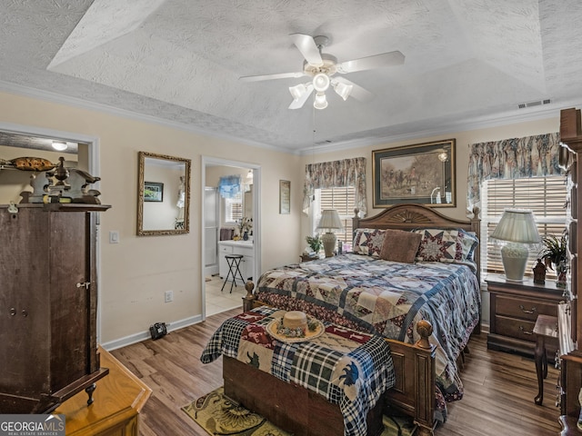 bedroom with baseboards, a tray ceiling, ornamental molding, wood finished floors, and a textured ceiling