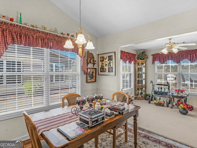carpeted dining space with lofted ceiling and ceiling fan with notable chandelier