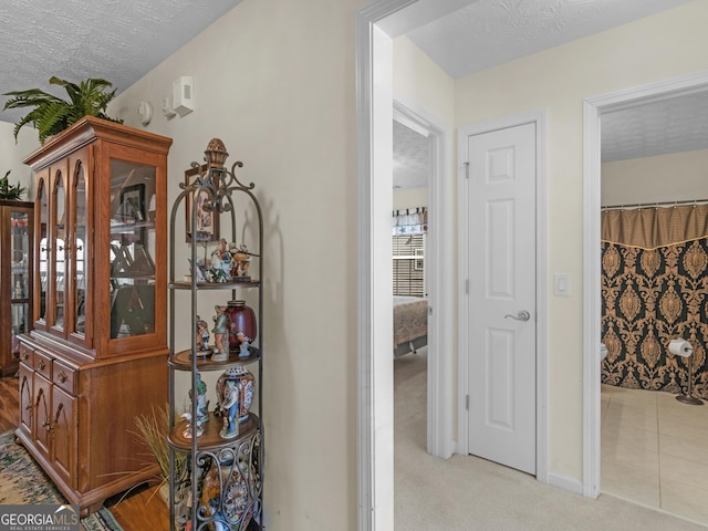 hallway with light colored carpet and a textured ceiling