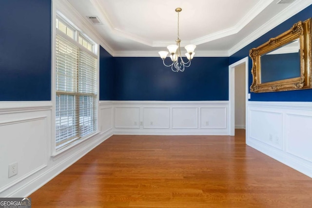 unfurnished dining area with crown molding, wainscoting, wood finished floors, and a chandelier