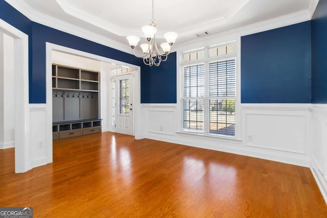 unfurnished dining area featuring ornamental molding, wainscoting, a decorative wall, wood finished floors, and a notable chandelier