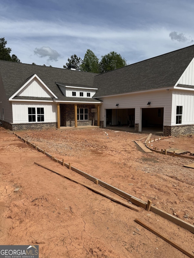 view of front of home featuring board and batten siding, an attached garage, brick siding, dirt driveway, and roof with shingles