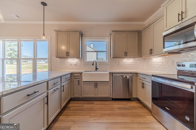 kitchen featuring appliances with stainless steel finishes, a sink, ornamental molding, tasteful backsplash, and light stone counters