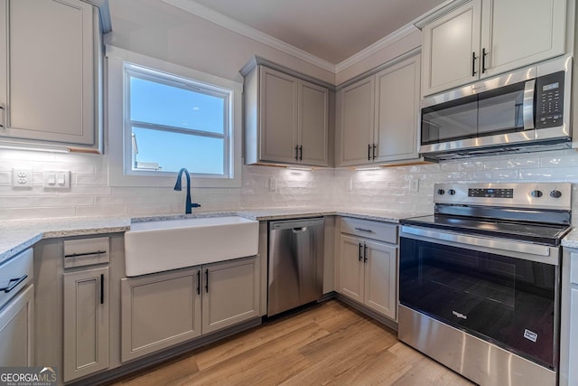 kitchen featuring stainless steel appliances, a sink, gray cabinetry, ornamental molding, and backsplash