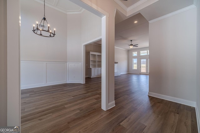 unfurnished dining area featuring a chandelier, ceiling fan, dark wood-style flooring, crown molding, and baseboards