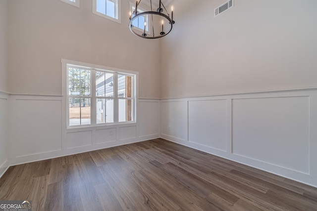 unfurnished dining area with a decorative wall, plenty of natural light, a chandelier, wainscoting, and dark wood-type flooring