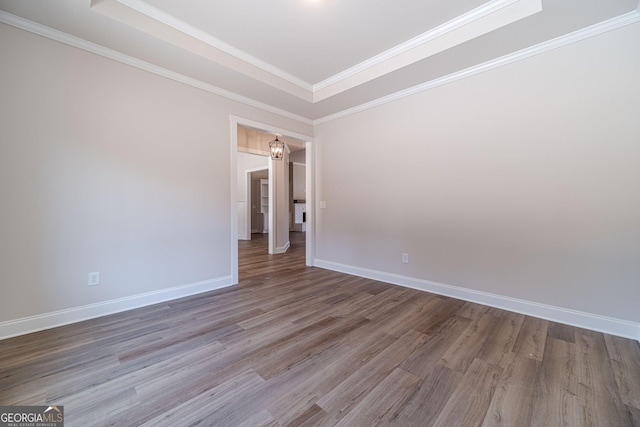 spare room featuring wood finished floors, a tray ceiling, baseboards, and crown molding