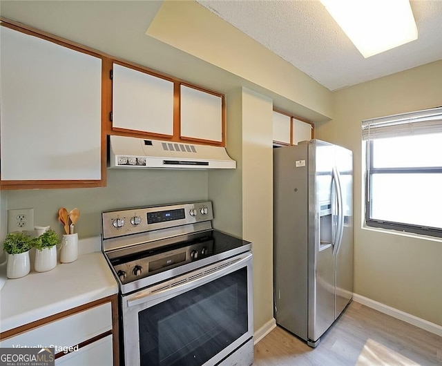 kitchen with light countertops, appliances with stainless steel finishes, under cabinet range hood, light wood finished floors, and white cabinetry