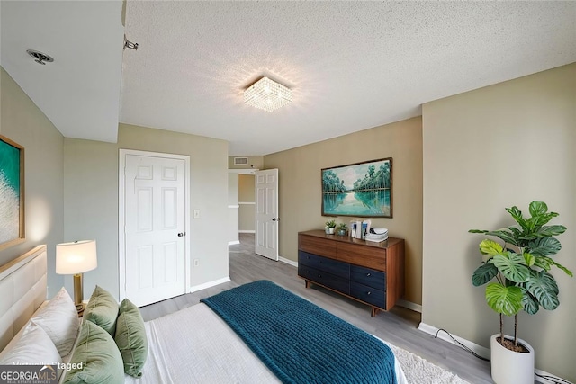 bedroom with visible vents, baseboards, wood finished floors, and a textured ceiling