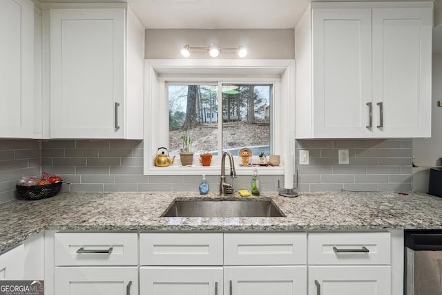 kitchen featuring light stone counters, white cabinetry, tasteful backsplash, and a sink