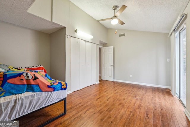 bedroom with vaulted ceiling, wood finished floors, visible vents, and a closet