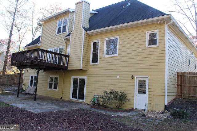 rear view of property featuring a patio, a shingled roof, a chimney, and fence