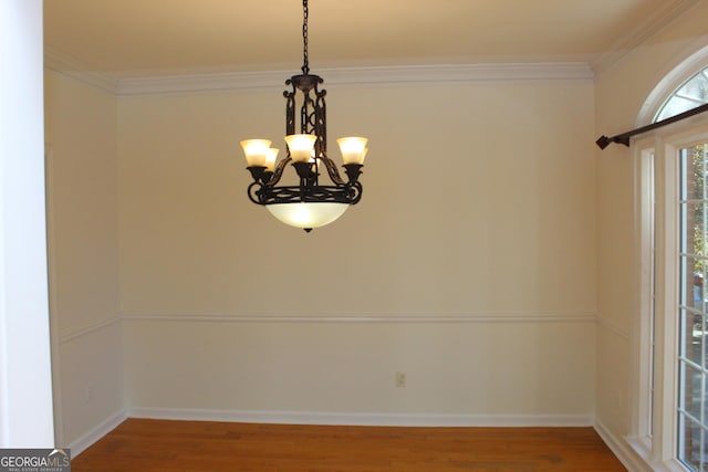 unfurnished dining area featuring crown molding, a notable chandelier, wood finished floors, and baseboards