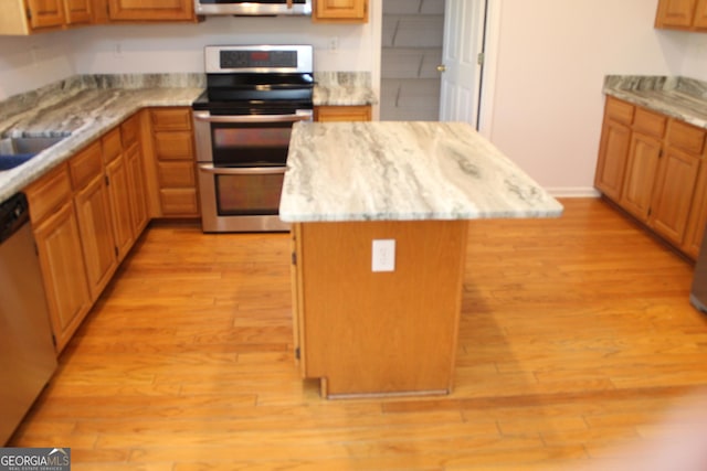 kitchen with brown cabinetry, appliances with stainless steel finishes, a center island, and light wood-style floors
