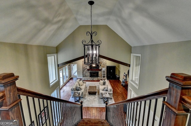 stairs featuring high vaulted ceiling, a stone fireplace, an inviting chandelier, and wood finished floors