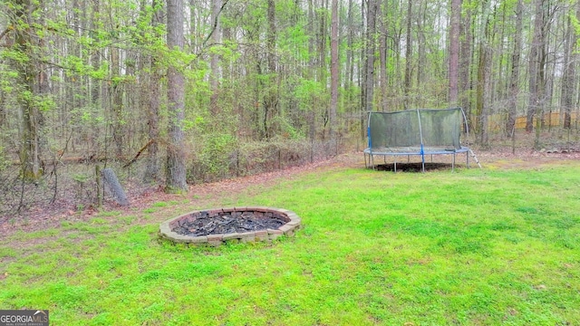 view of yard with a trampoline, a fire pit, and a wooded view