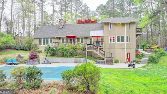 rear view of house with a chimney, a covered pool, stairway, a patio area, and a lawn