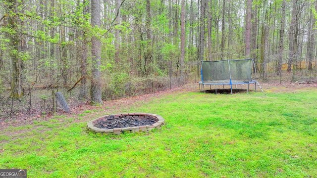 view of yard featuring an outdoor fire pit, a view of trees, and a trampoline
