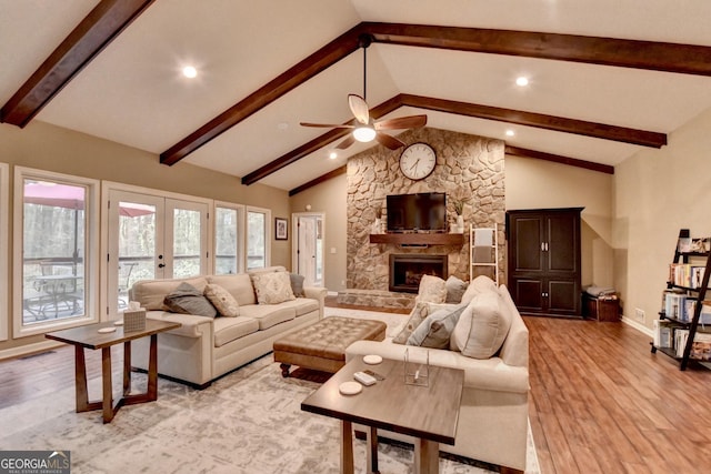 living area featuring beamed ceiling, light wood finished floors, a stone fireplace, and a ceiling fan