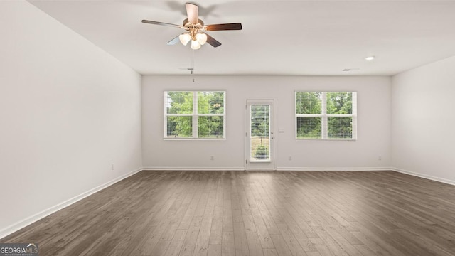 empty room with a healthy amount of sunlight, a ceiling fan, baseboards, and dark wood-style flooring